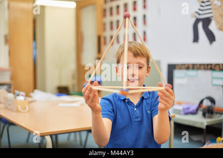 Primary schoolboy holding up plastic straw pyramid in classroom Stock Photo