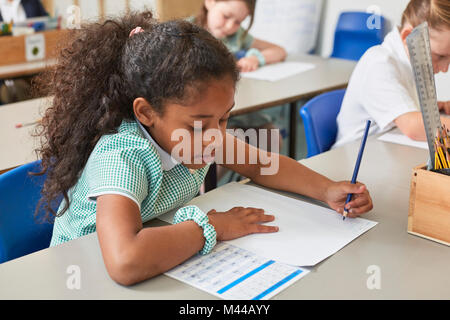 Schoolgirl writing at classroom desk in primary school lesson Stock Photo