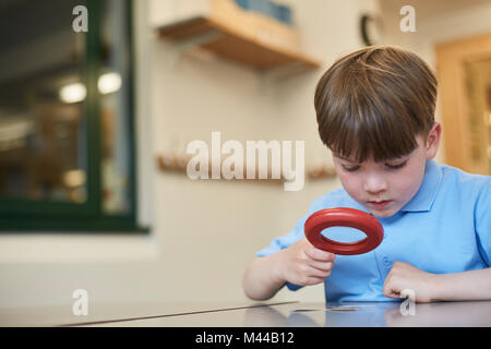 Schoolboy looking through magnifying glass in classroom lesson at primary school Stock Photo