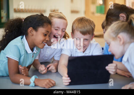 Schoolboys and girls laughing at digital tablet in classroom at primary school Stock Photo