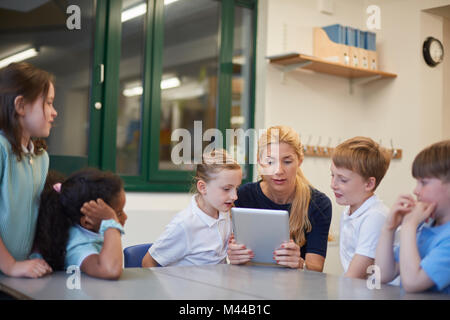 Teacher with schoolboys and girls looking at digital tablet in classroom at primary school