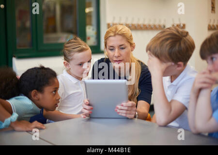 Teacher with schoolgirls and boys looking at digital tablet in classroom at primary school Stock Photo
