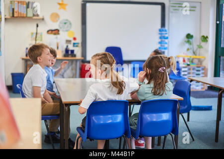 Schoolgirls and boys around classroom table primary school Stock Photo