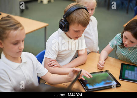 Schoolboys and girls looking at digital tablets in class at primary school Stock Photo
