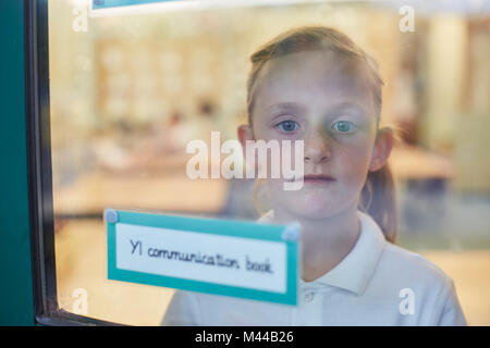 Portrait of schoolgirl looking through classroom window at primary school Stock Photo