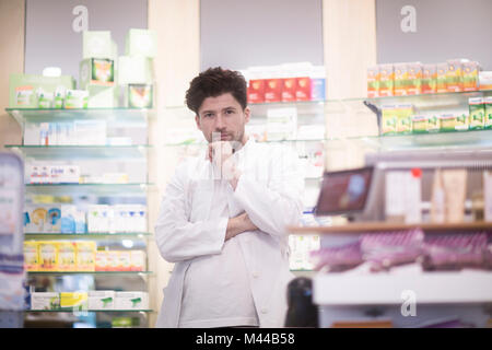 Portrait of young male pharmacist with hand on chin in pharmacy Stock Photo