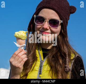 Outdoor closeup fashion portrait of young hipster crazy girl eating ice cream in summer hot weather in round mirror sunglasses have fun and good mood. Toned style instagram filters Stock Photo