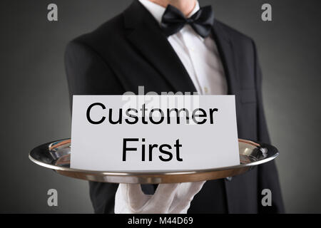 Close-up Of A Male Waiter Holding Tray With Text Customer First On Card Stock Photo