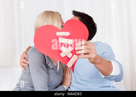 Kissing Couple Holding Paper Red Heart Fixed With Plaster Bandage In Front Of Their Faces Stock Photo
