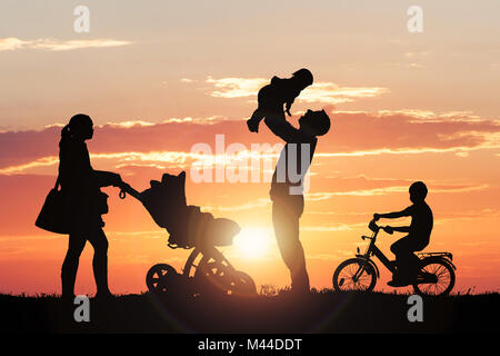 Family Silhouette Enjoying At Park Against Dramatic Sky During Sunset Stock Photo
