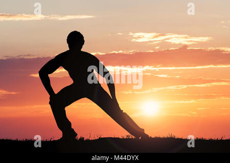 Silhouette Of A Man Doing Exercise Against Dramatic Sky At Sunset Stock Photo