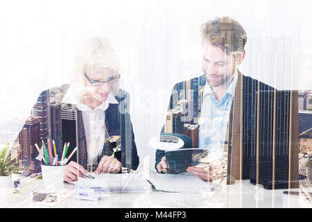 Double exposure of male and female colleagues working at desk over city background Stock Photo