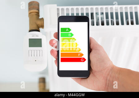 Closeup of man's hand using energy label on mobile phone against radiator at home Stock Photo