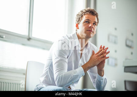Thoughtful young businessman with hands clasped sitting in office Stock Photo