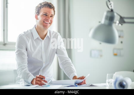 Smiling young businessman analyzing documents in office Stock Photo