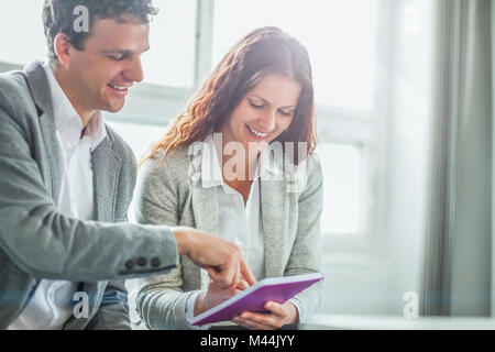 Young businessman pointing on book while female colleague writing in office Stock Photo