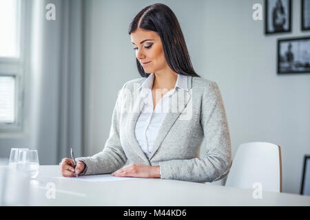 Beautiful young businesswoman writing on document in office Stock Photo