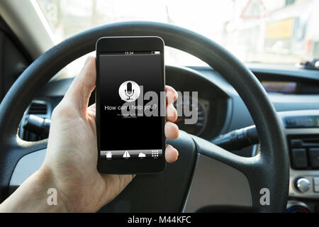 Hand holding smart phone with how can I help you? text on screen in car Stock Photo