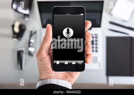 How can I help you? text on smart phone screen held by businessman in office Stock Photo