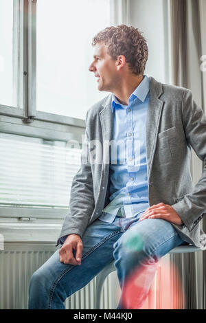 Thoughtful young businessman looking through office window Stock Photo