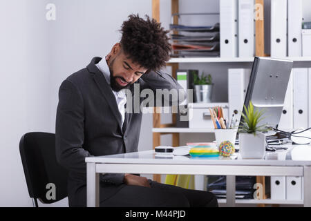 Young Businessman Suffering From Neck Pain Sitting In Office Stock Photo