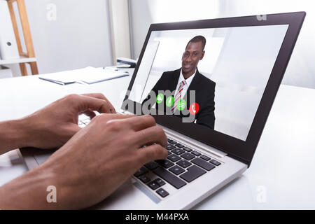 Close-up Of A Businessperson's Hand Video Conferencing With Male Colleague On Laptop At Workplace Stock Photo