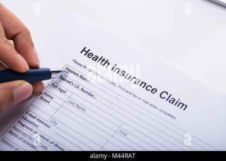 Close-up Of A Human Hand Filling Health Insurance Claim Form With Pen Stock Photo