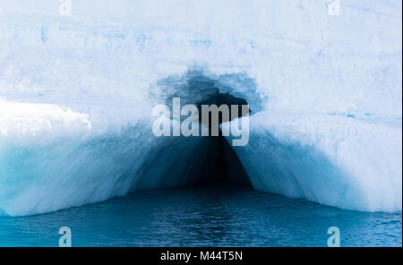 A deep turquoise blue keyhole entrance into an iceberg in the lighter turquoise blue Southern Ocean surrounding the Antarctic Peninsula. Stock Photo