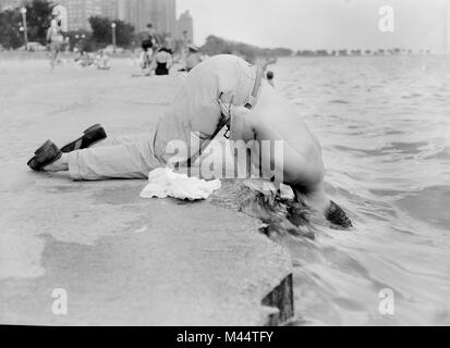 A man cools off along Oak Street beach in Chicago by sticking his head in Lake MIchigan, ca. 1955. Stock Photo