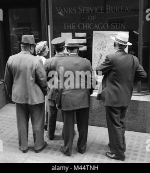 A crowd gathers in front of a World War II news update in the Yanks Service Bureau window of the Chicago Sun, ca. 1944. Stock Photo