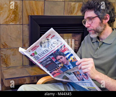 Man reading a newspaper at home.  Middle aged Caucasian man reading the Vancouver Sun newspaper at home. Stock Photo