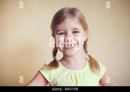 Happy lost tooth little girl portrait, studio shoot on the yellow background Stock Photo