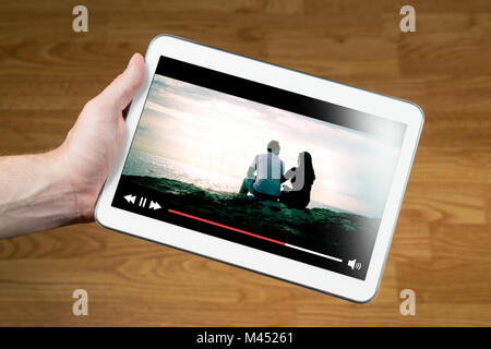 Man watching movie online with mobile device. Hand holding tablet with imaginary video player and film streaming service. Stock Photo