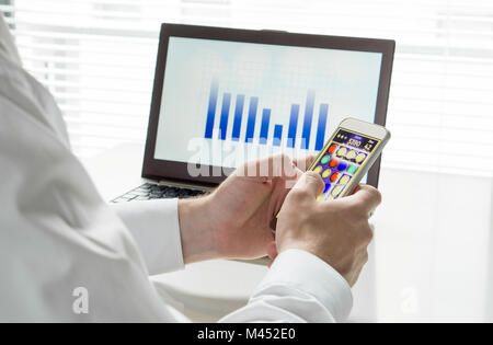 Lazy and unproductive office worker playing mobile game with smartphone during work hours. Avoiding his job with laptop and business figures. Stock Photo