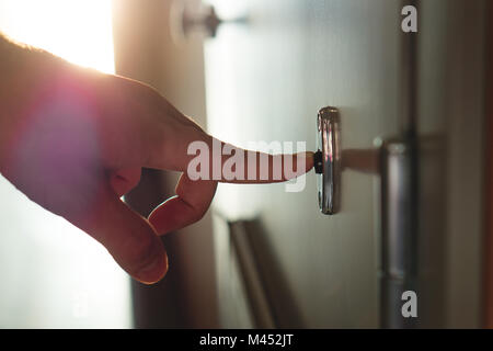 Finger pressing doorbell in sunny apartment building corridor. Close up of male hand ringing door bell in a block of flats. Salesman, fundraiser. Stock Photo