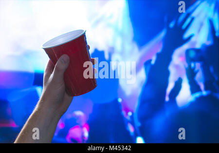 Young man holding red party cup in nightclub dance floor. Alcohol container in hand in disco. College student having fun and dancing. Stock Photo