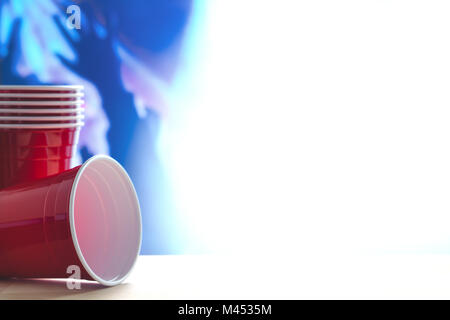 Red party cups themed background. People dancing hands up in the air in the blurred blue background. Containers stacked. Empty blank white copy space  Stock Photo