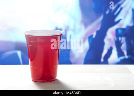 Plastic red party cup on a table. Nightclub full of people dancing on the dance floor in the background. Disco lighting. Perfect for marketing. Stock Photo