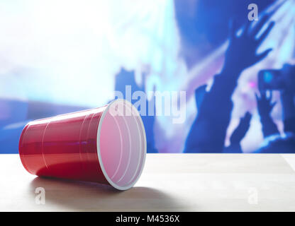 Fallen plastic red party cup on its side on a table. Nightclub or disco full of people dancing on the dance floor in the background. Stock Photo
