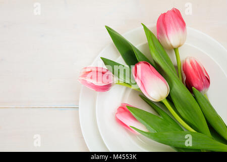 Valentines day concept. Pink tulips on white plates, white wooden background. Top view Stock Photo