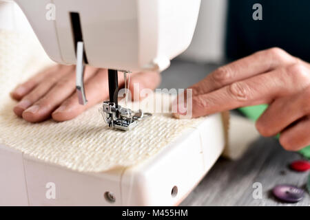 closeup of a young caucasian man sewing a beige fabric with a sewing machine Stock Photo