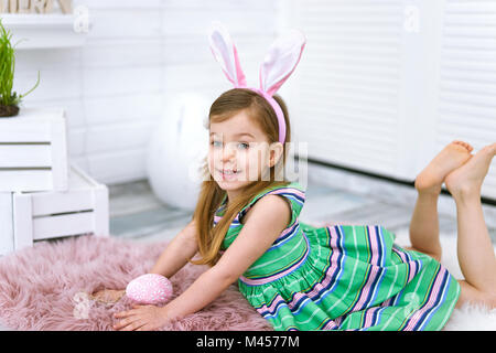 Close up of four years old girl with bunny ears and big egg in her hands on white background around Easter decorations Stock Photo