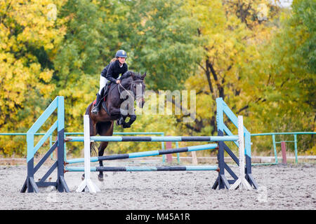 Young rider girl on bay horse jumping over barrier on equestrian sport competition. Horseback girl on show jumping contest Stock Photo