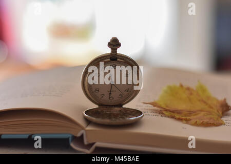 Old pocket watch and opened book on the table/ Sunday relaxing and still life concept. Selective focus. Stock Photo