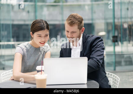 Young businessman and woman looking at laptop at sidewalk cafe meeting Stock Photo