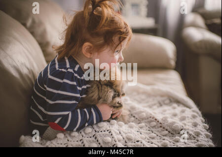 Young girl sitting on sofa, hugging pet dog Stock Photo