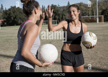 Women on football pitch with football, doing high five Stock Photo
