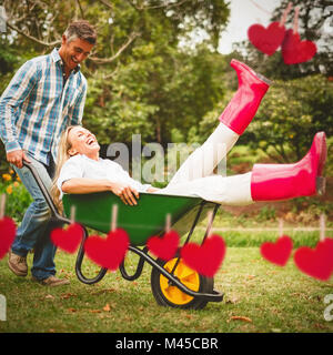 Composite image of happy couple playing with a wheelbarrow Stock Photo