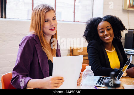 Colleagues working together at desk, looking away smiling Stock Photo