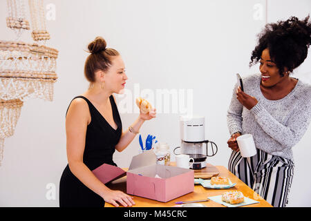 Woman photographing friend eating doughnut Stock Photo